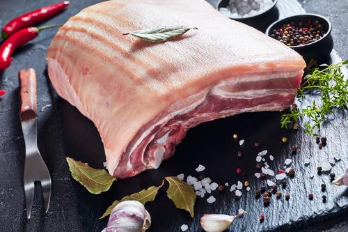 raw pork belly with skin on a black slate tray with spices and herbs