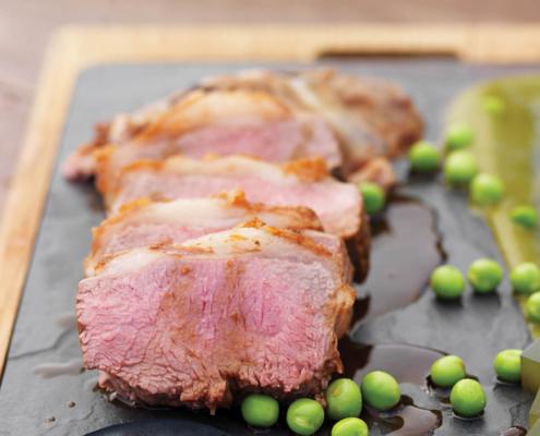 A cannon of lamb on a slate with peas.
