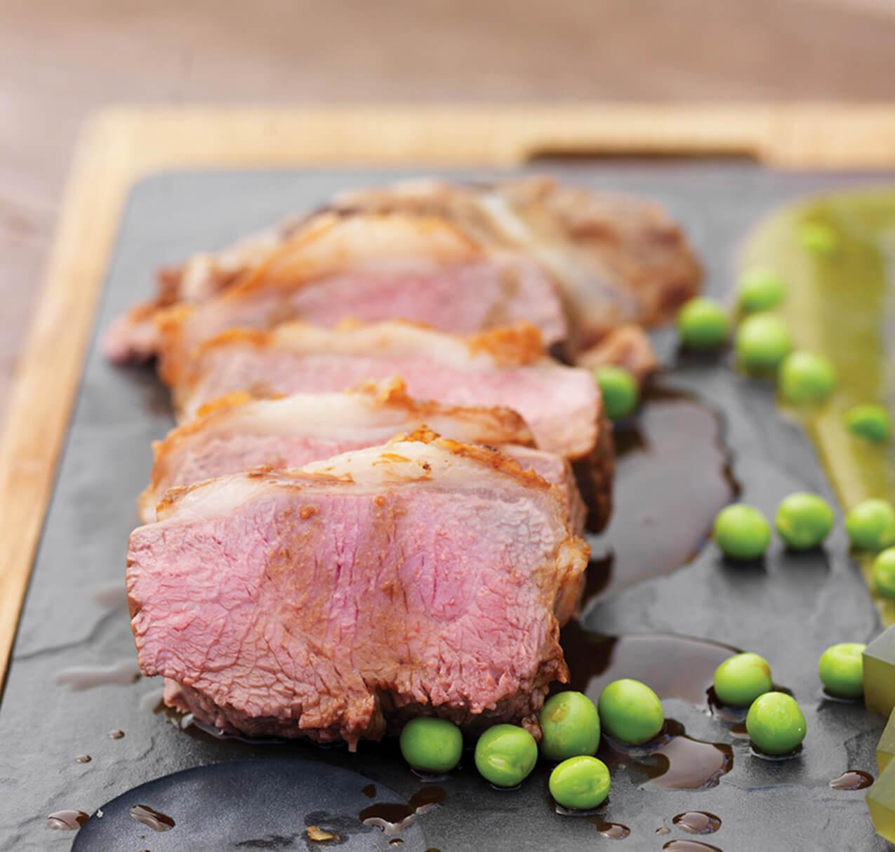 A cannon of lamb on a slate with peas.